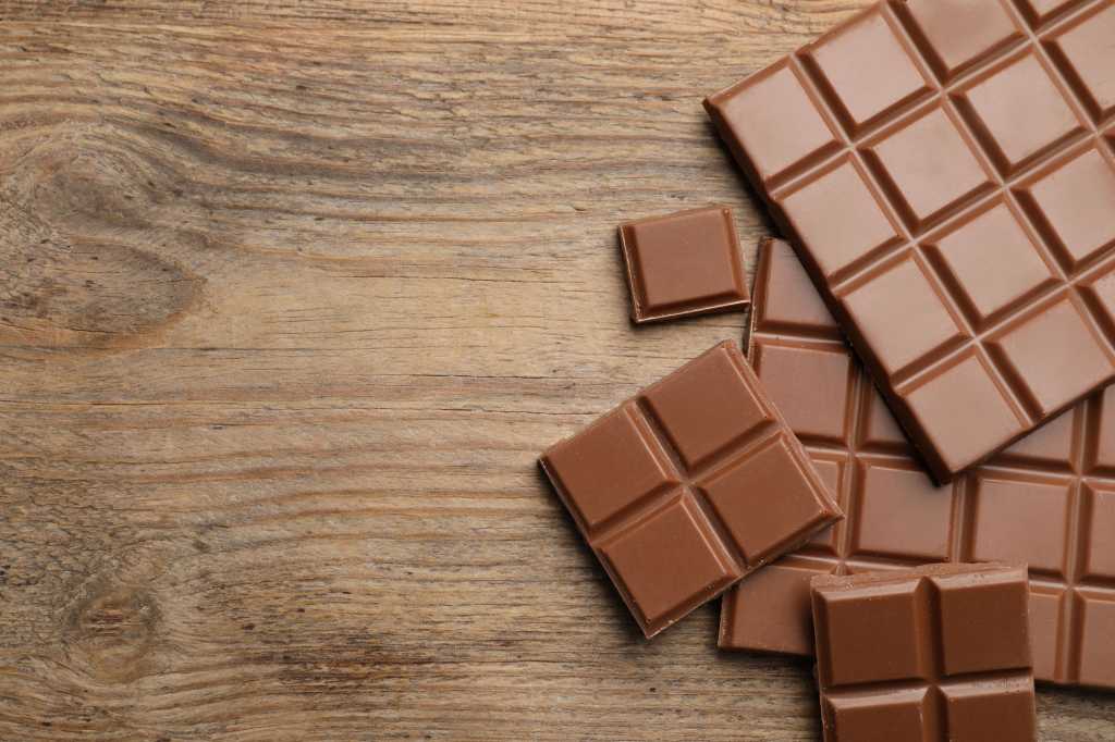 Milk chocolate squares on a wooden table. Chunks of various sizes. Overhead view.